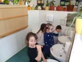 Učenje pravilnega čiščenja svojih zob v umivalnici ob ogledalu z zobnimi ščetkami, prinesenimi od doma